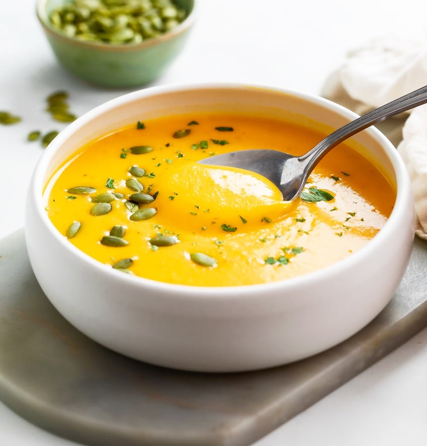Roasted Butternut Squash Soup in a white bowl with a spoon and pumpkin seeds on top.