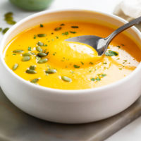 A white bowl filled with Roasted Butternut Squash Soup with pumpkin seeds and parsley on top.