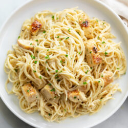 A white plate with angel hair pasta with chicken.