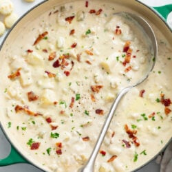 Clam Chowder in a soup pot with a spoon on the side and chopped bacon on top.