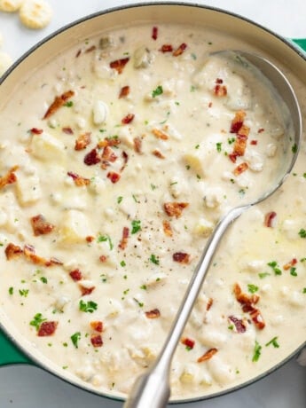 Clam Chowder in a soup pot with a spoon on the side and chopped bacon on top.