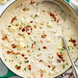 A soup pot filled with creamy New England Clam Chowder with bacon and parsley on top.