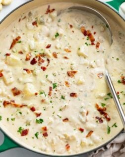 A soup pot filled with creamy New England Clam Chowder with bacon and parsley on top.