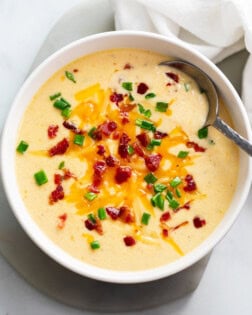 Beer Cheese Soup in a white bowl with bacon, cheese, and green onions on top.