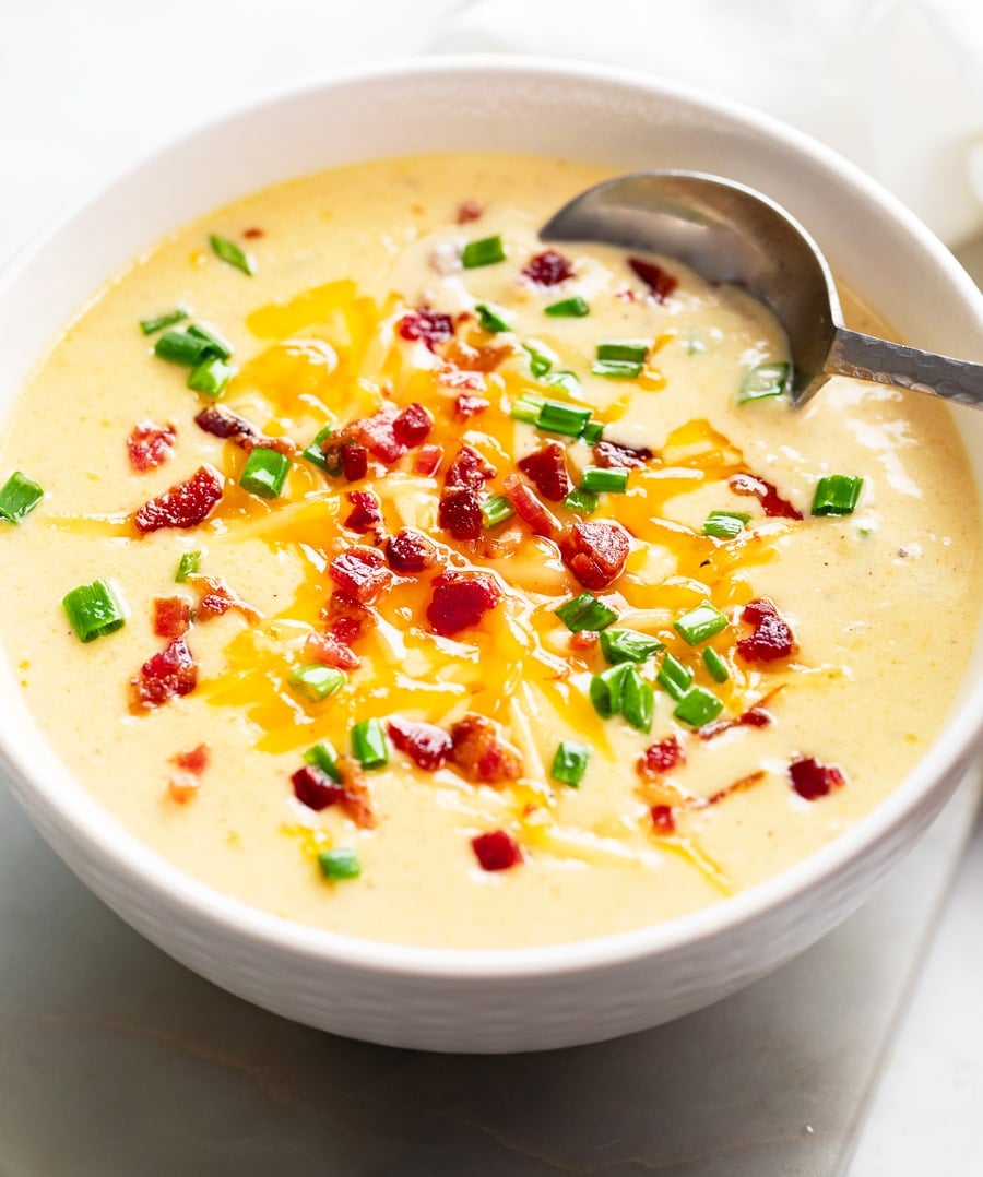 A white bowl with Beer Cheese Soup with bacon, cheese, and chives.