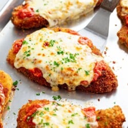 A spatula lifting up a piece of chicken parmesan.