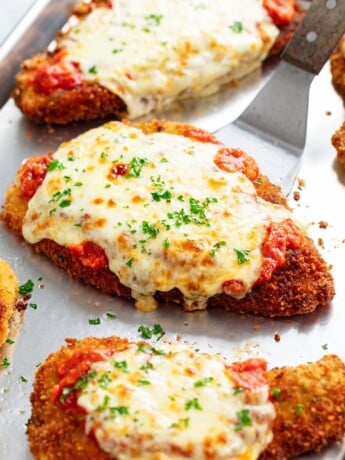 A spatula lifting up a piece of chicken parmesan.