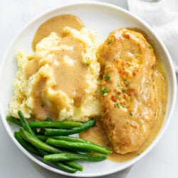 A white plate with chicken and gravy with mashed potatoes and green beans.