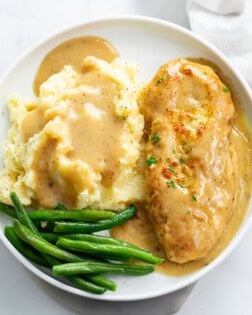 A white plate with chicken and gravy with mashed potatoes and green beans.