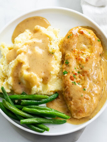 A white plate with chicken and gravy with mashed potatoes and green beans.