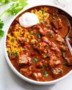 A white bowl filled with Chili Con Carne with cheese and sour cream.