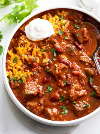 A white bowl filled with Chili Con Carne with cheese and sour cream.