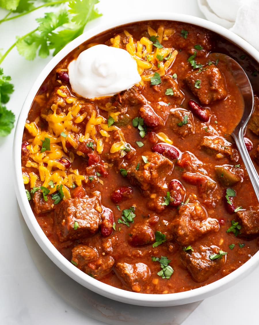 A white bowl filled with Chili Con Carne with cheese and sour cream.