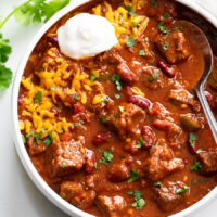 Chili Con Carne in a white bowl with shredded cheese and sour cream on top.