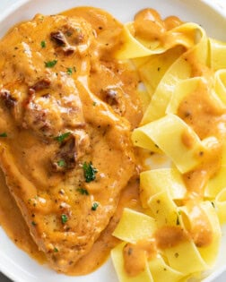 A white plate with Marry Me Chicken with a side of pappardelle pasta.