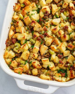 A white casserole dish with sausage stuffing with parsley on top.