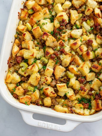 A white casserole dish with sausage stuffing with parsley on top.