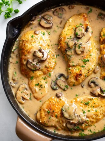 Chicken Marsala in a skillet with marsala sauce, mushrooms, and parsley.