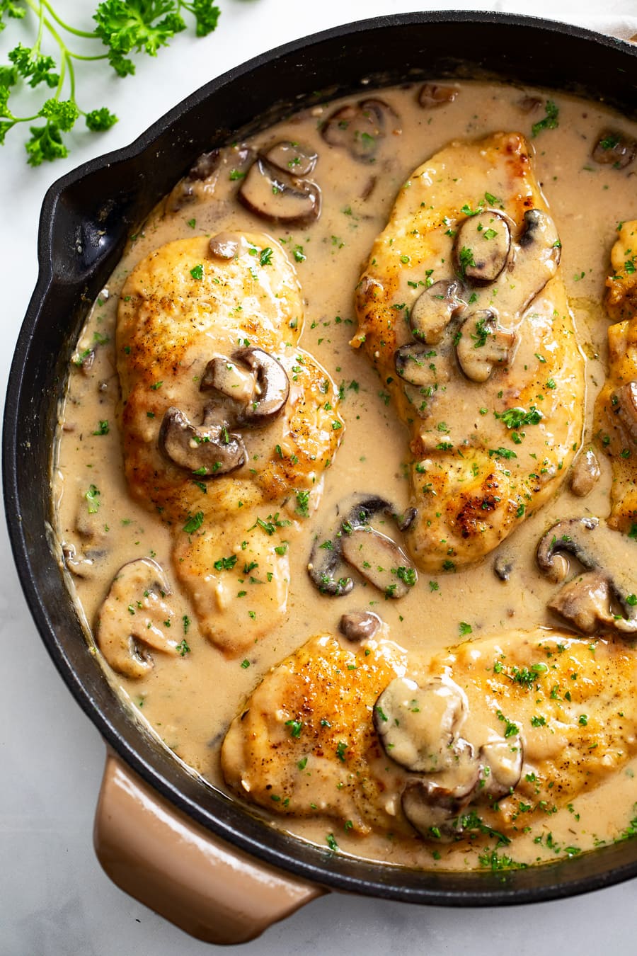 Chicken Marsala in a skillet with marsala sauce, mushrooms, and parsley. 