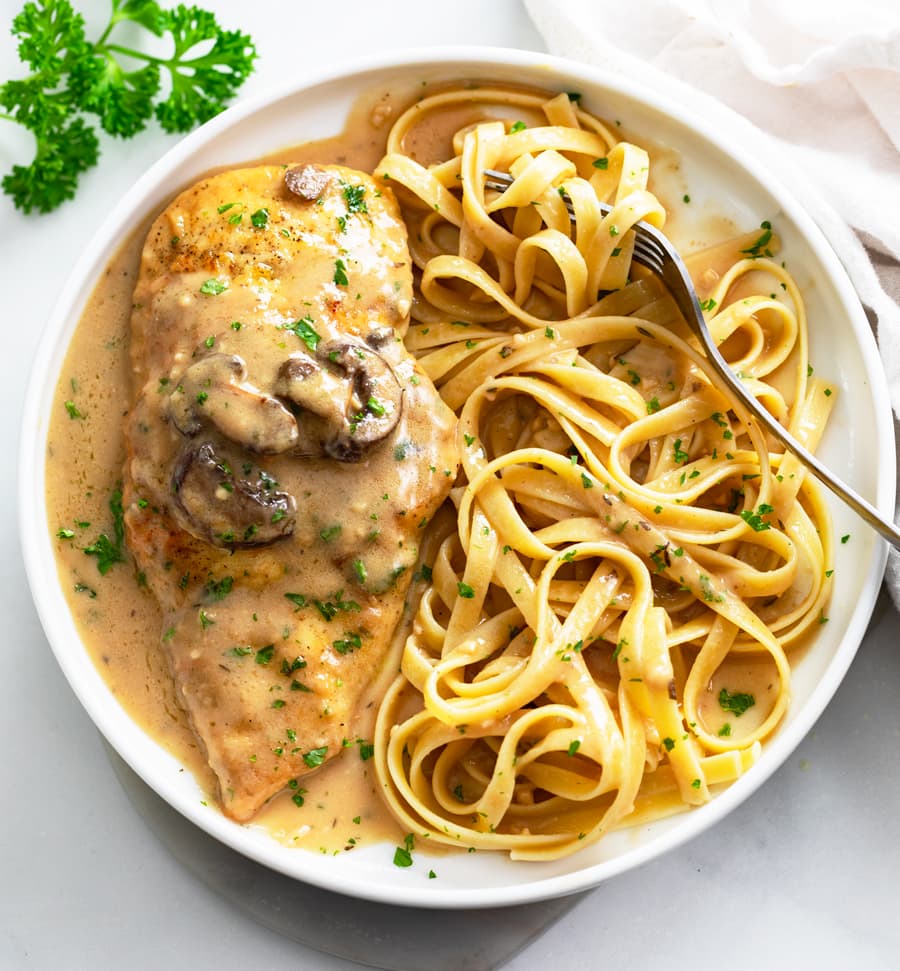 A white plate with Chicken Marsala and Fettuccine Pasta.