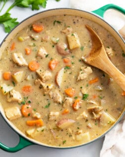 A Dutch oven filled with Chicken Stew with a wooden spoon in it.