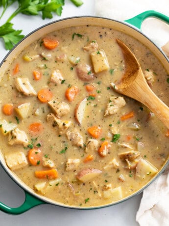 A Dutch oven filled with Chicken Stew with a wooden spoon in it.