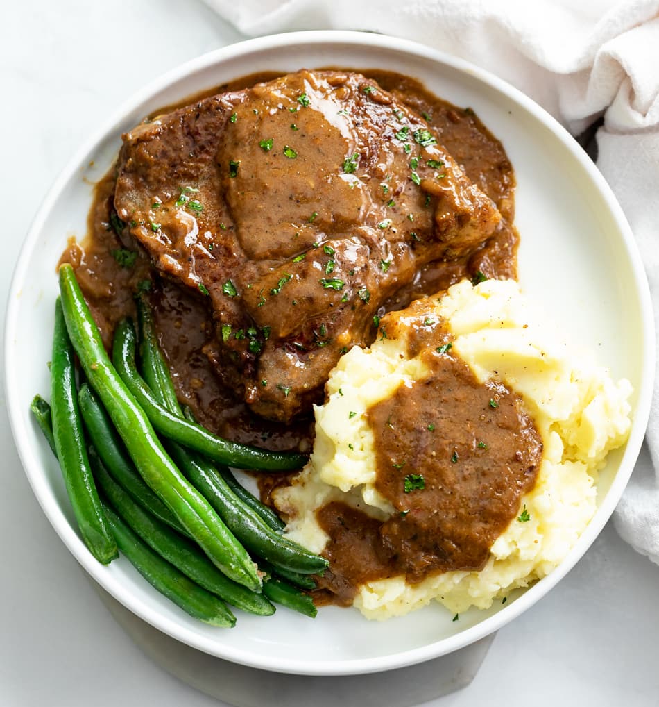 Steak with Gravy, mashed potatoes, and green beans on a white plate.