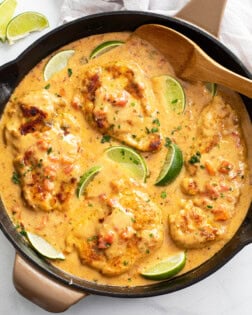 Cajun Chicken in a skillet with sauce and lime wedges with fresh cilantro.