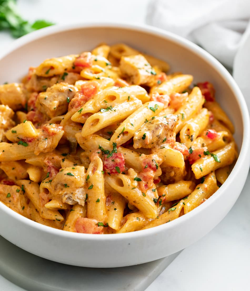 A white bowl of Cajun Chicken Pasta with diced tomatoes and penne pasta.
