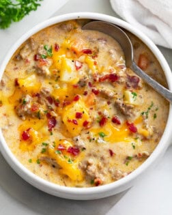 A white bowl filled with Cheeseburger Soup with a spoon on the side.