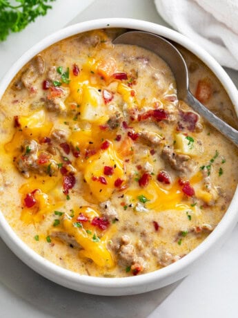 A white bowl filled with Cheeseburger Soup with a spoon on the side.