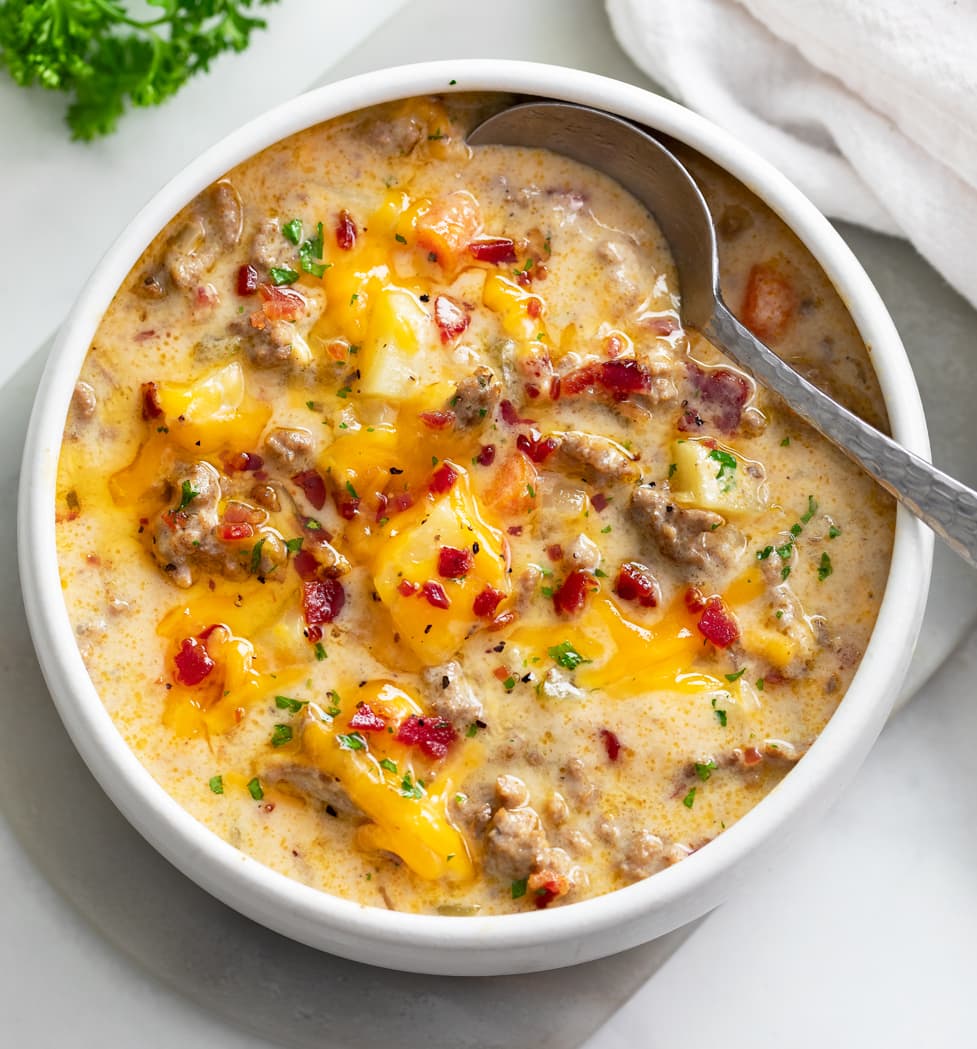 A white bowl filled with Cheeseburger Soup with a spoon on the side.