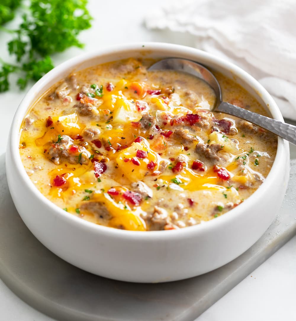Cheeseburger Soup in a white bowl with a spoon and bacon on top.