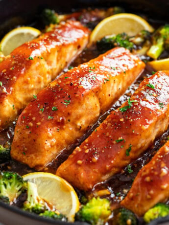 Honey Glazed Salmon in a skillet with broccoli and lemon wedges.