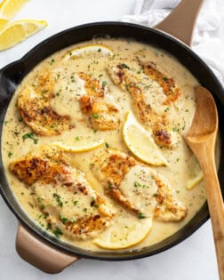 A skillet of Lemon Pepper Chicken in a sauce with a wooden spoon on the side.