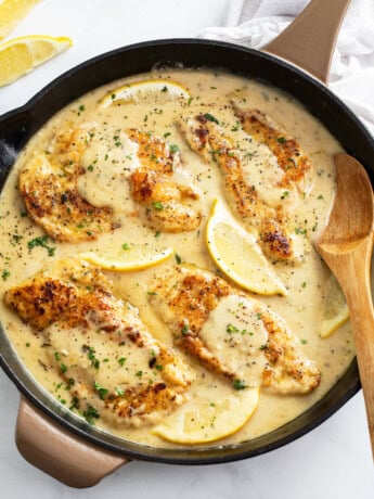 A skillet of Lemon Pepper Chicken in a sauce with a wooden spoon on the side.