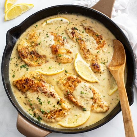 A skillet of Lemon Pepper Chicken in a sauce with a wooden spoon on the side.