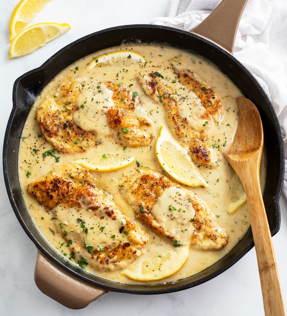 A skillet of Lemon Pepper Chicken in a sauce with a wooden spoon on the side.