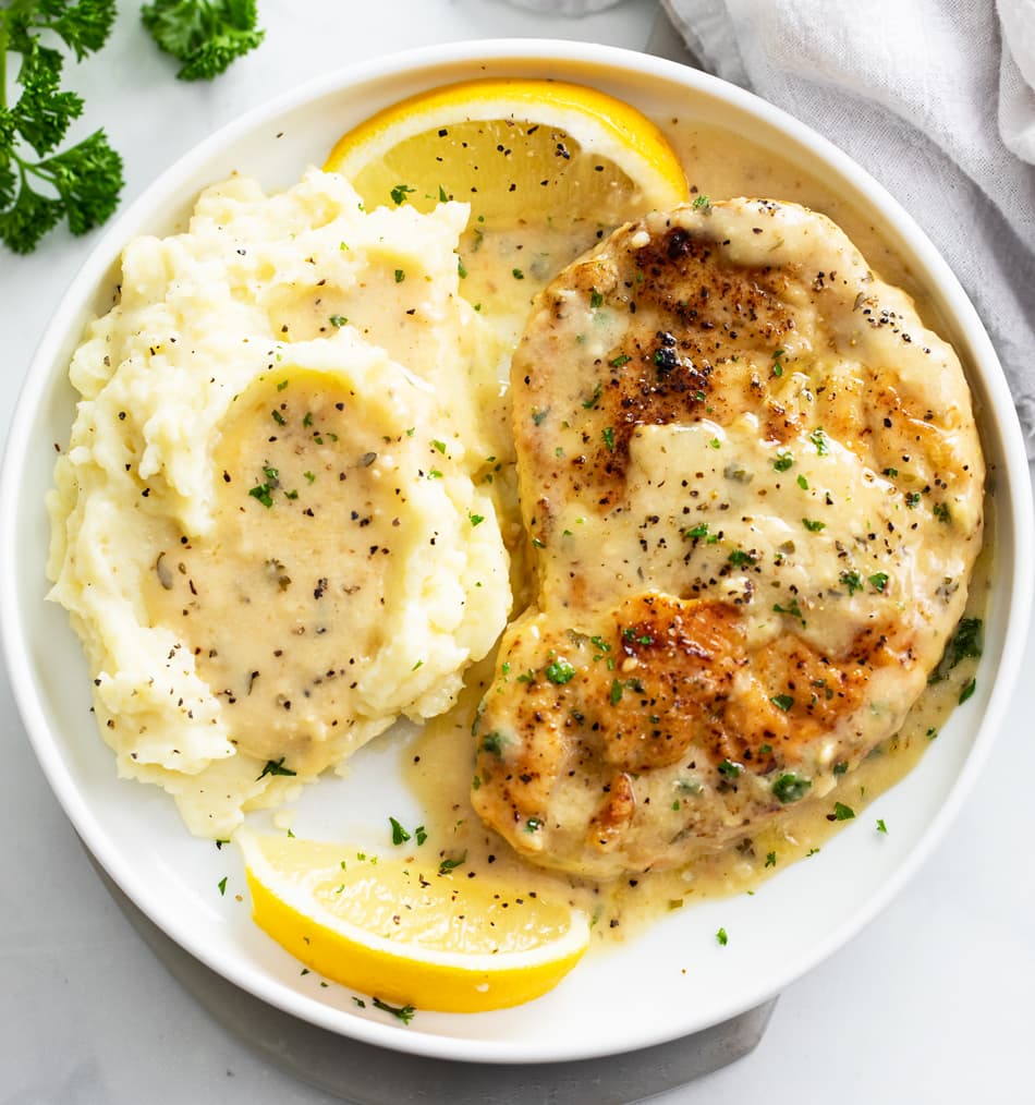 Lemon Pepper Chicken on a white plate with mashed potatoes and lemon slices.