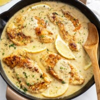 A skillet with Lemon Pepper Chicken in a sauce with lemon wedges and parsley.