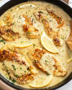 A skillet with Lemon Pepper Chicken in a sauce with lemon wedges and parsley.