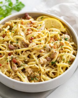 A white bowl of Linguine with Clams with lemon wedges on the side.