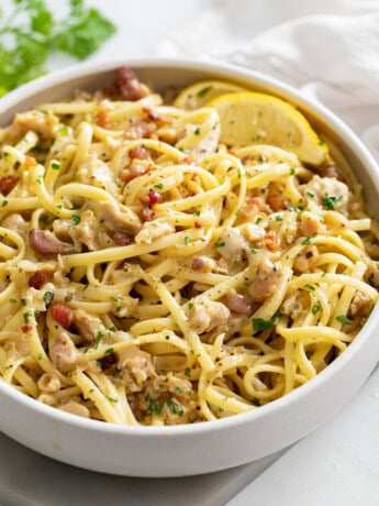 A white bowl of Linguine with Clams with lemon wedges on the side.