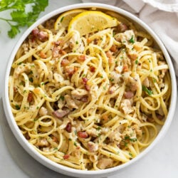 A white bowl filled with Linguine with Clams with lemon wedges and parsley.