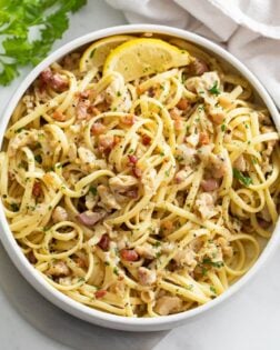 A white bowl filled with Linguine with Clams with lemon wedges and parsley.