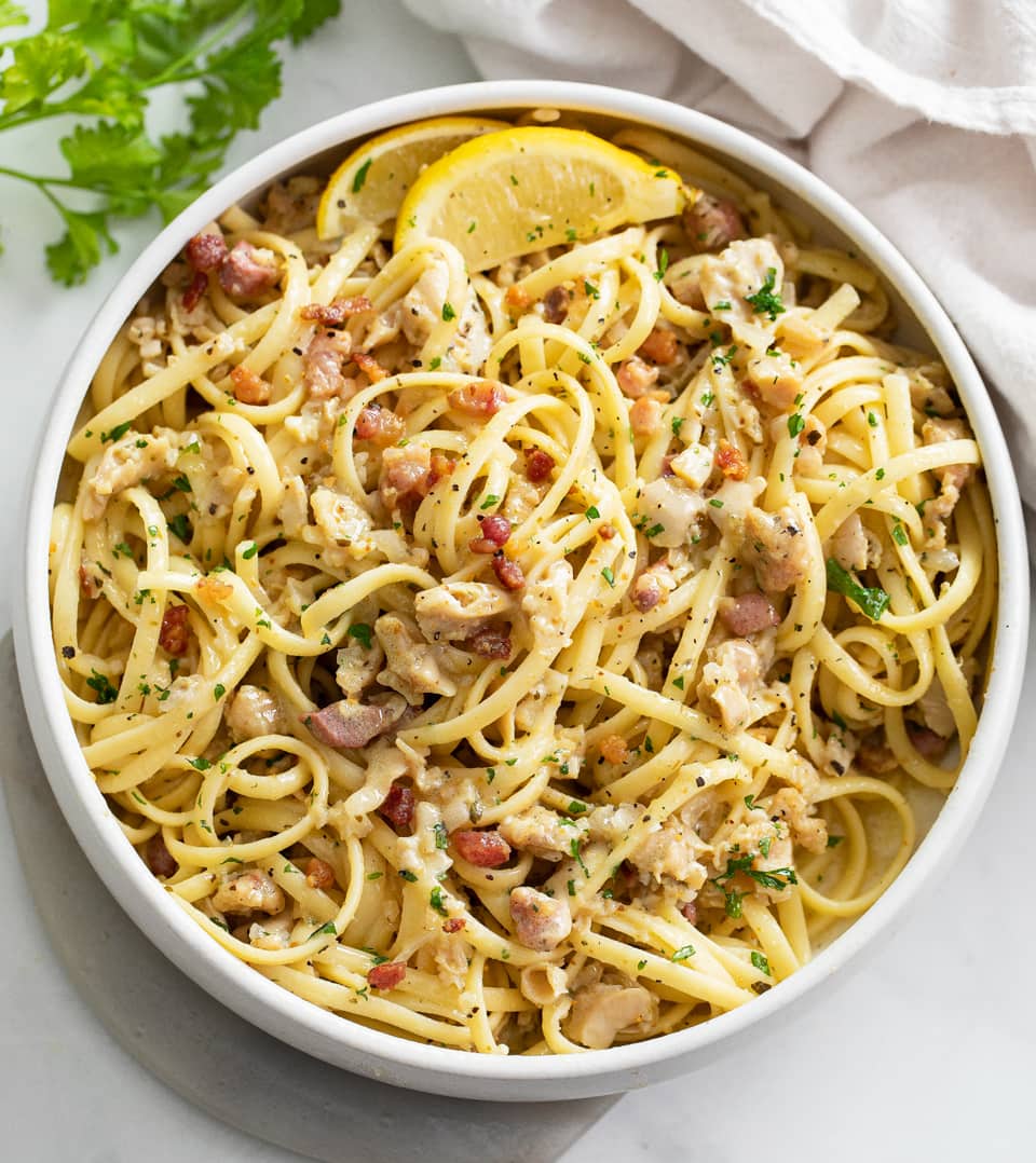 A white bowl filled with Linguine with Clams with lemon wedges and parsley.