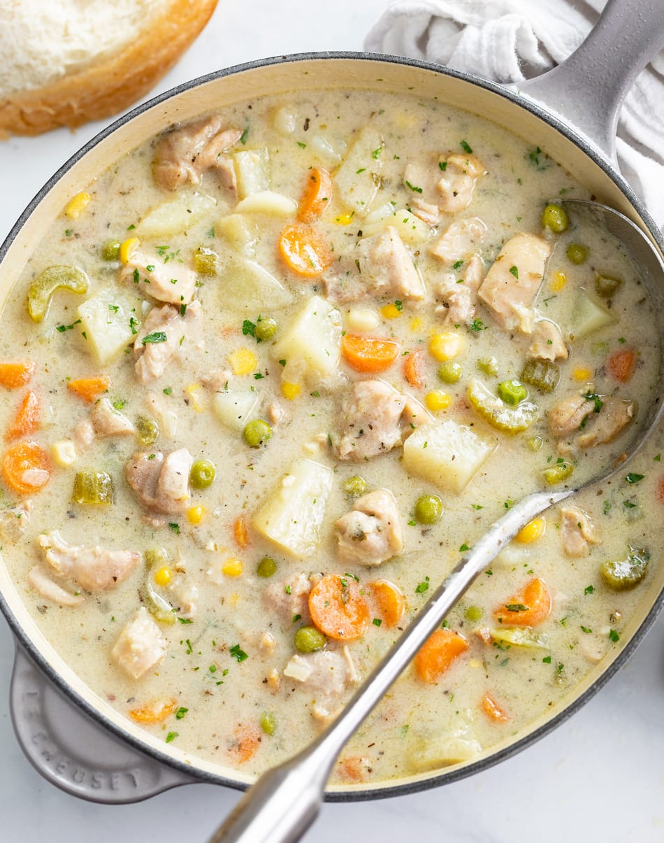 A soup pot filled with Creamy Chicken Soup with a ladle on the side.