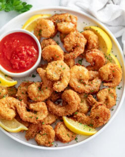 A pile of Fried Shrimp on a white plate with lemon slices and sauce.