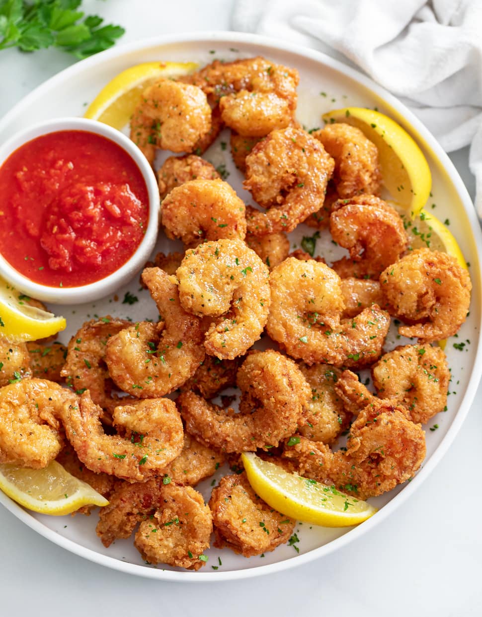 A pile of Fried Shrimp on a white plate with lemon slices and sauce.