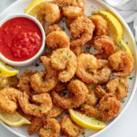 Fried Shrimp on a white plate with sauce and slices of lemon.